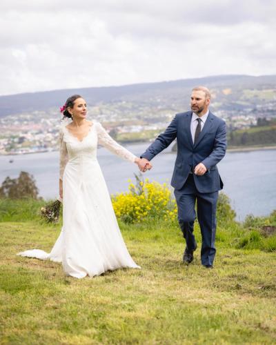 a bride and groom walking on a hill holding hands at Hotel Parque Quilquico in Castro