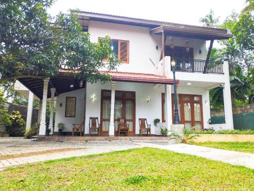 a white house with a balcony and a yard at Villa Muthuwin in Panadura