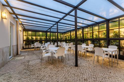 a conservatory with white tables and chairs and windows at Hotel Avenida Park in Lisbon