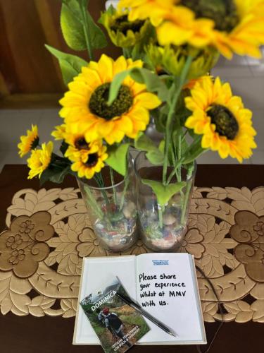 a table with a vase with sunflowers and a book at Matthew's Miracle View in Roseau