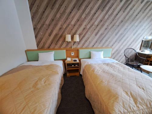 two beds in a room with a wooden ceiling at Business Hotel Kawakami in Kumano