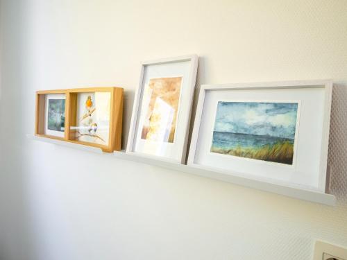 three framed photographs on a white shelf on a wall at Stylish Retreat with Sauna in Awenne