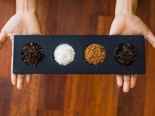 a person holding a black plate with four different types of food at The Leaf Jimbaran in Jimbaran