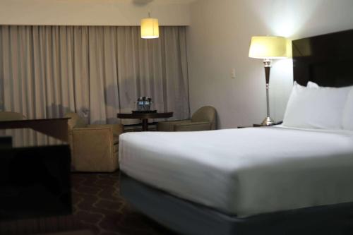 a hotel room with a large white bed and a chair at Wyndham Garden Los Mochis Plaza Inn in Los Mochis