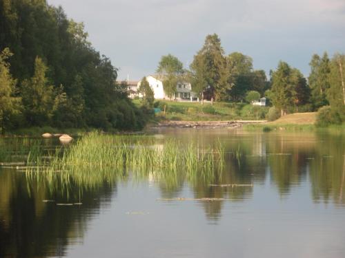 a lake with trees and a house in the background at Maalaiskartano Pihkala in Kestilä
