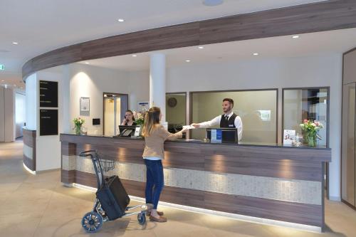 a woman is standing at a bar with a man behind a counter at Best Western Queens Hotel Pforzheim-Niefern in Pforzheim