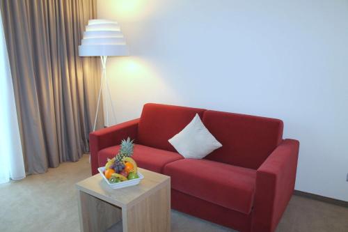 a living room with a red couch and a table with a bowl of fruit at Best Western Queens Hotel Pforzheim-Niefern in Pforzheim