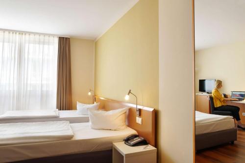 a hotel room with two beds and a woman sitting in a chair at Best Western Macrander Hotel Dresden in Dresden