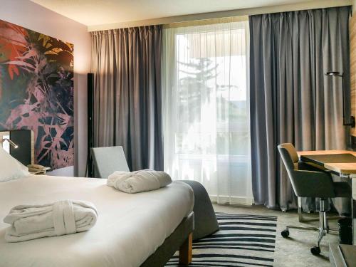 a hotel room with a bed and a desk and a window at Novotel Narbonne Sud A9/A61 in Narbonne