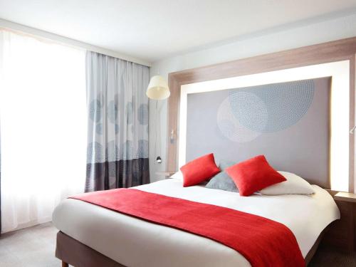 a bedroom with a large bed with red pillows at Novotel Narbonne Sud A9/A61 in Narbonne
