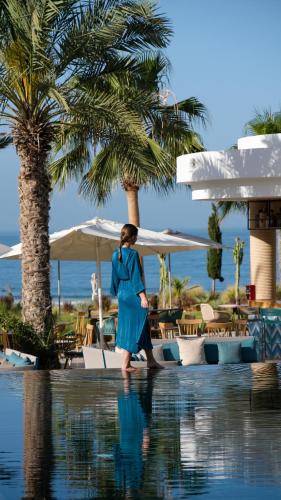 a woman in a blue dress walking by a swimming pool at Hyatt Regency Taghazout in Taghazout