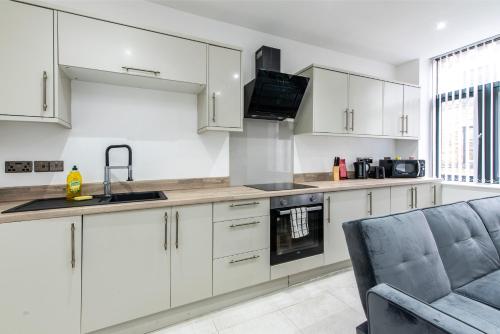 eine Küche mit weißen Schränken, einer Spüle und einer Couch in der Unterkunft 1-Bed Apartment near Bradford City Centre in Bradford