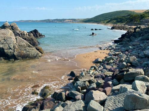 a beach with rocks and people swimming in the water at The Tall Barn in Rose Ash