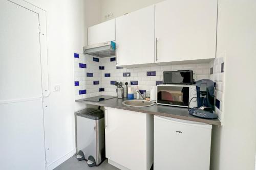 une cuisine avec des placards blancs et un comptoir avec un four micro-ondes dans l'établissement Flexliving - Studio - Parodi, à Paris