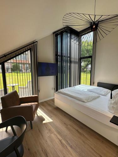 a bedroom with a bed and a chair and windows at STADE LAND GOLF HOTEL & Tiny Houses in Deinste