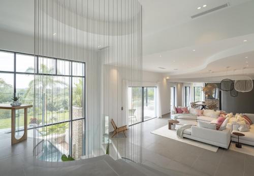 Elle comprend un salon doté d'un mobilier blanc et de grandes fenêtres. dans l'établissement Villa Bella Vista - New luxury villa, à Roquefort-les-Pins