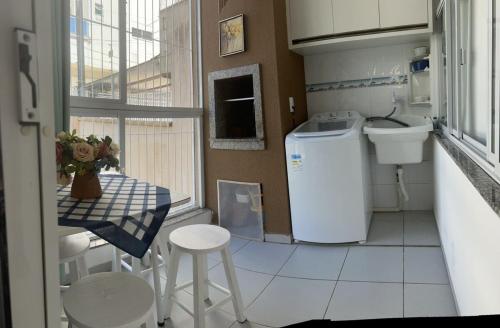 una pequeña cocina con fregadero, mesa y taburete en Apartamento Itapema centro, en Itapema