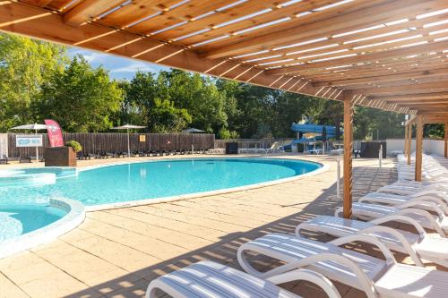 a swimming pool with white chairs and a wooden pergola at Camping Clos Cottet in Angles