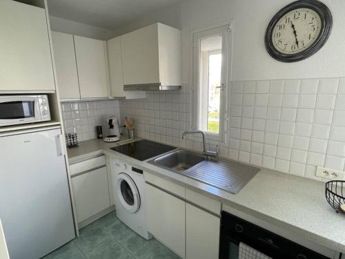 une cuisine avec un évier et une horloge murale dans l'établissement Appartement tout confort, à 200m de la plage avec parking privé et piscine - FR-1-723-64, au Cap d'Agde