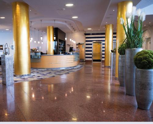 a lobby with yellow columns and plants in pots at Vitalia Seehotel in Bad Segeberg