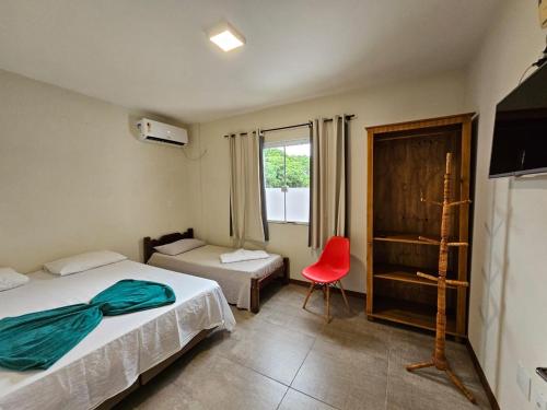 a bedroom with two beds and a red chair at Morada da Figueira in Bombinhas