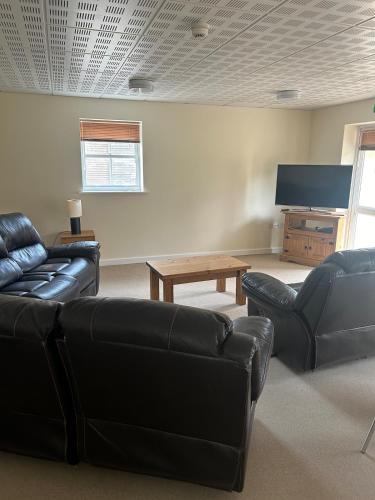 a living room with black leather furniture and a flat screen tv at Forest holiday home with option to bring your horse & Hot Tub in Brettenham