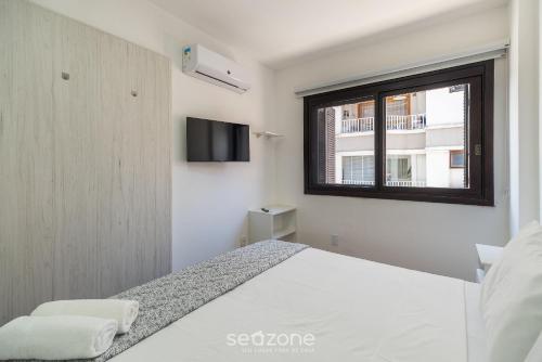 a white bedroom with a bed and a window at Apto c/ Churrasqueira 450m da Praia PNM0202 in Florianópolis
