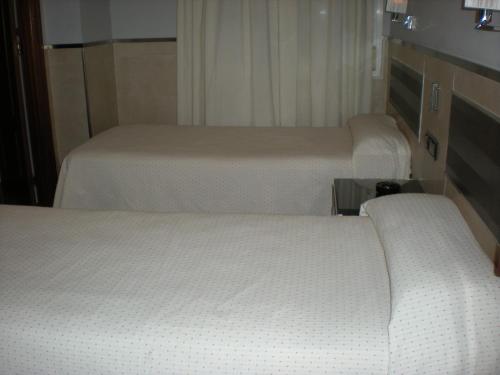three beds in a room with white sheets at Hostal La Hispanidad in Málaga