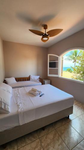 a bedroom with a bed with a ceiling fan and a window at Pousada Flor de Lótus Caraguá in Caraguatatuba