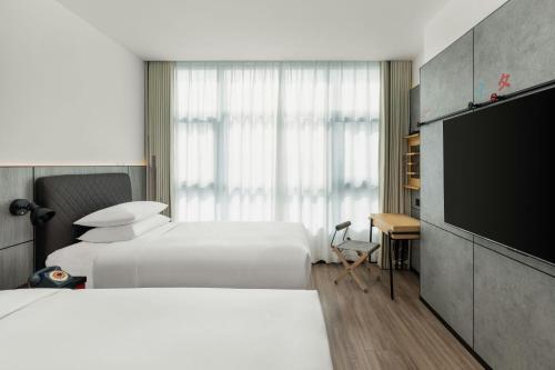 a hotel room with two beds and a flat screen tv at Moxy Suzhou City Centre in Suzhou