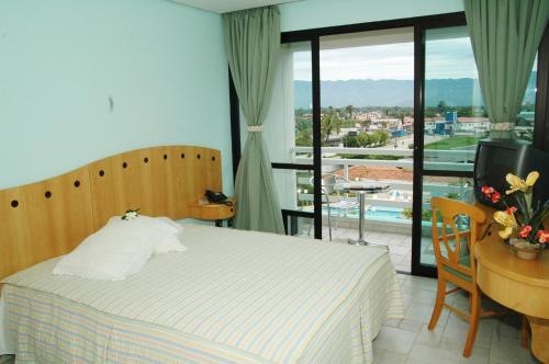 a bedroom with a bed and a television and a balcony at Hotel Aojesp in Caraguatatuba