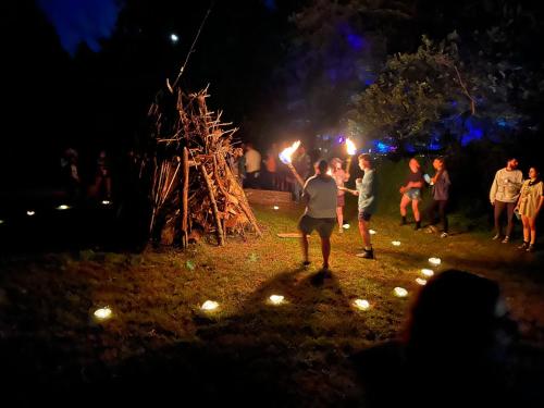 a group of people standing around a bonfire at night at Slumberland at the River's Edge in Pond Eddy