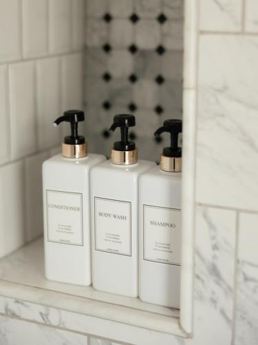 three bottles of soap on a shelf in a bathroom at Designer Home, Hot Tub, Private Yard, & Projector in Hudson