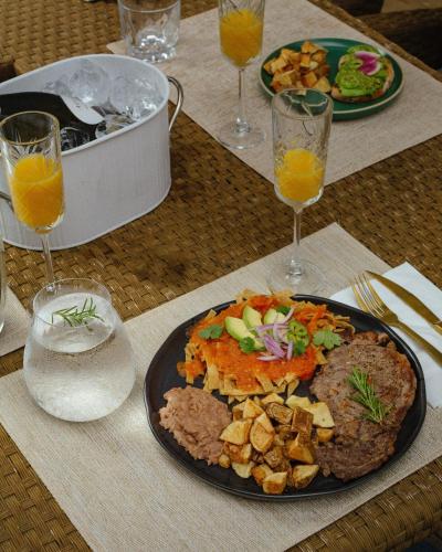a table with a plate of food and glasses of orange juice at Boskenvid Hotel - Romantic Treehouses & Skypool in Valle de Guadalupe