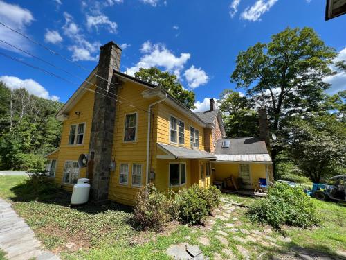 a yellow house with a chimney on a yard at Slumberland at the River's Edge in Pond Eddy