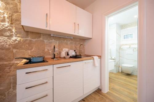 a kitchen with white cabinets and a stone wall at Apartment Villa IV in Trogir