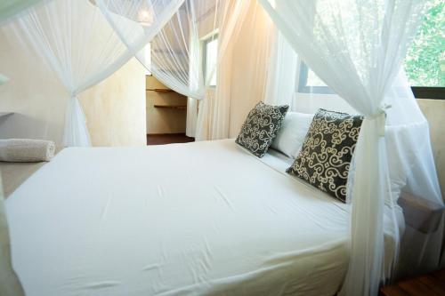a bedroom with a white bed with curtains and a window at Tree House Cottage, Garden Views, Hot Water in Praia do Tofo