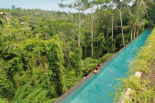 a woman sitting on the edge of a pool in the jungle at The Hidden Paradise Ubud - CHSE Certified in Ubud
