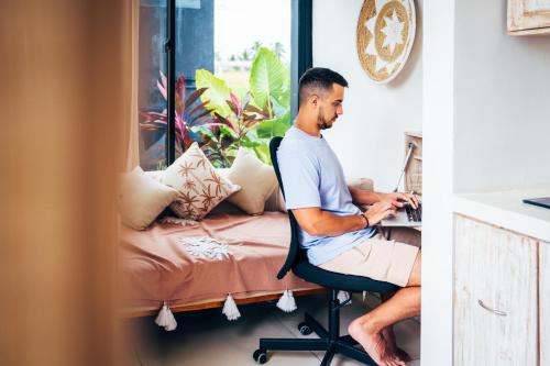 un homme assis sur une chaise travaillant sur un ordinateur portable dans l'établissement Wander Havens, à Canggu