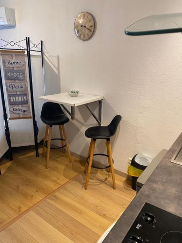 a table with two chairs and a clock on the wall at Nancy, Magnifique studio totalement climatisé, meublé, salle de bains et wc séparés, parking privé, cuisine équipée, WIFI in Malzéville