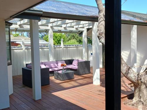 a patio with a purple couch on a wooden deck at Doonside Private Cottage at Grossi Point Reserve in Mapua