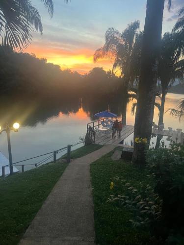 a pathway next to a body of water with a sunset at Las Palmas - Espectacular casa a borde de lago con piscina in Prado