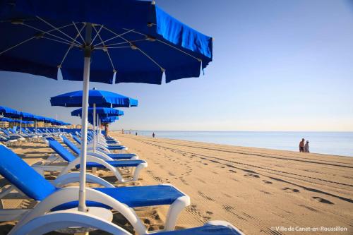 a row of blue chairs and umbrellas on a beach at T3 Vue Mer Clim Wifi Parking in Canet-en-Roussillon