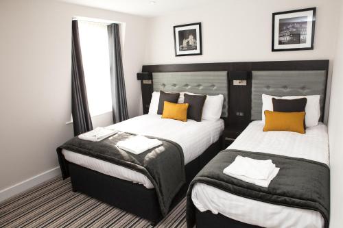 ロンドンにあるザ チューダー イン ホテルのホテルルーム ベッド2台(オレンジの枕付)