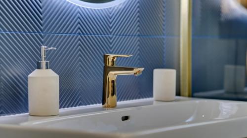 a bathroom sink with a gold faucet and a bottle of soap at Le Littoral - Appart'Escale in Saint-Nazaire