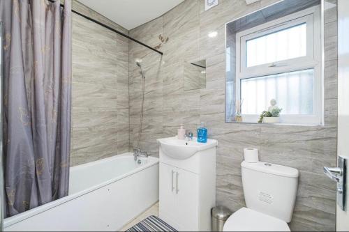 a bathroom with a toilet and a tub and a window at Contractor Haven, 6 bed house, sleeps 14 Parking x 2 WIFI Smart TV Central location in Goodmayes