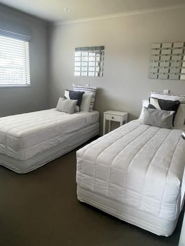 two beds in a bedroom with white walls at Ocean Breeze Resort Pauanui in Pauanui