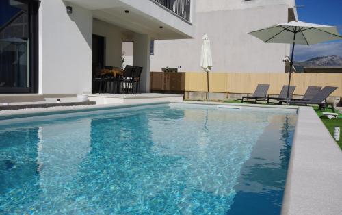 a swimming pool with an umbrella next to a house at PERISKA Home in Kaštela