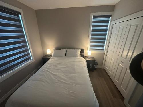 a bedroom with a bed with white sheets and two windows at Cozzy & Brand New Apartment, Near Banff Hwy in Calgary