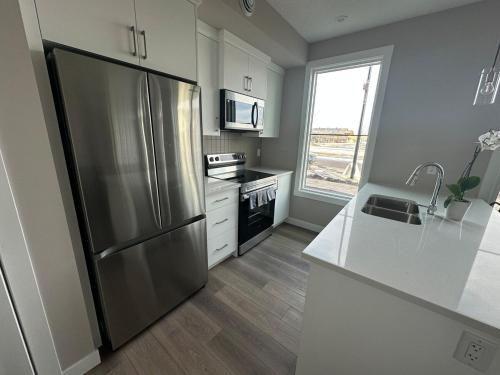 a kitchen with a stainless steel refrigerator and white cabinets at Cozzy & Brand New Apartment, Near Banff Hwy in Calgary